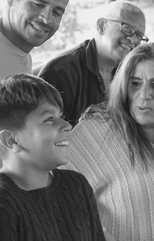 A group of people, including a smiling child and three adults, are gathered closely together, appearing to share a moment of joy, in a black and white image.