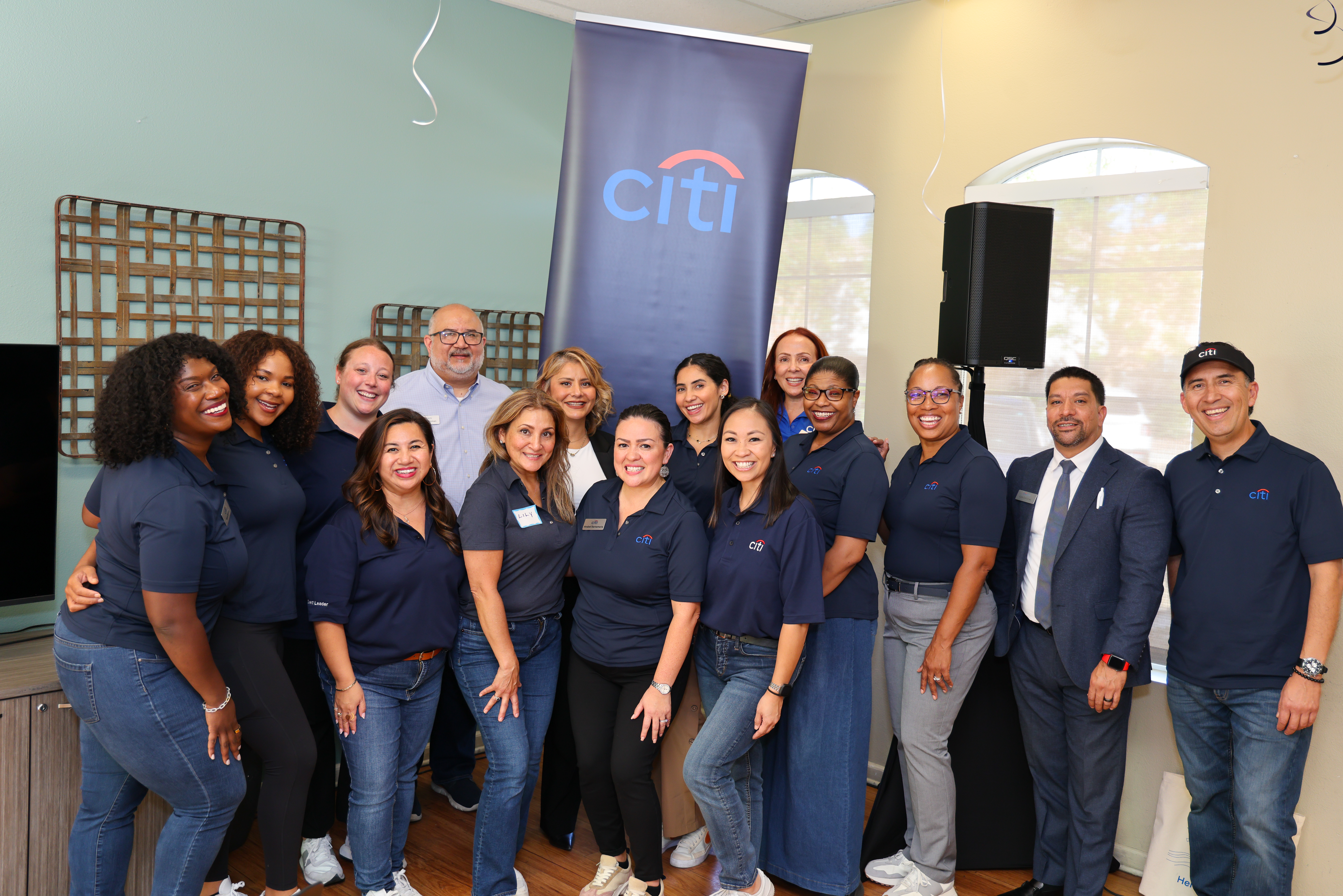 Seven Citi and 1 MoCaFi  staff stand in a row posing enthusiastically for a group photo in front of a PHIPPS-branded step-and-repeat banner.